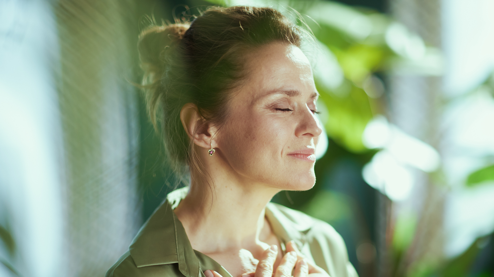 Woman standing with her eyes closed and a hand on her chest, taking a quiet moment during recovery