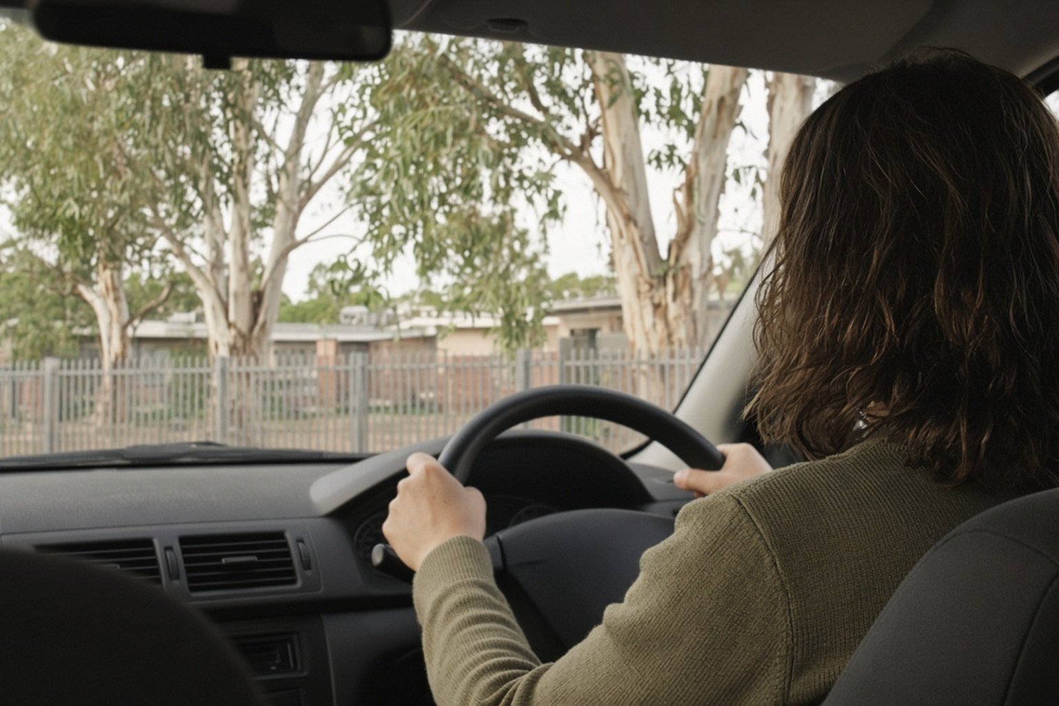 Woman sitting in her parked car outside a school, seen from behind